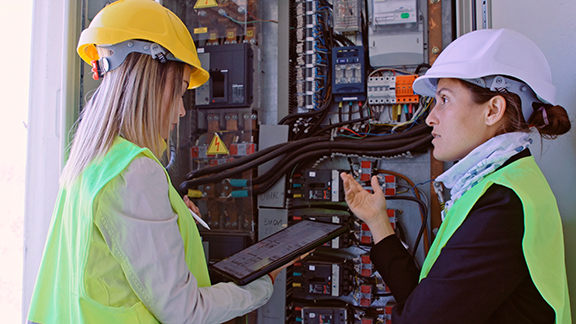 Two female maintenance engineers in front of a device, one of them holding a tablet